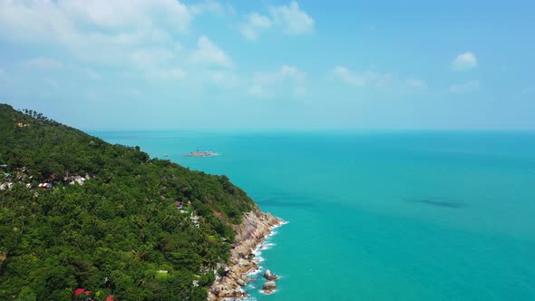 Tropical island panorama. Hilled shore with palm plantation, luxury resorts and calm turquoise sea.