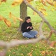 Happy Asian woman sitting and slide the screen on smartphone under tree at the park in Autumn - VideoHive Item for Sale