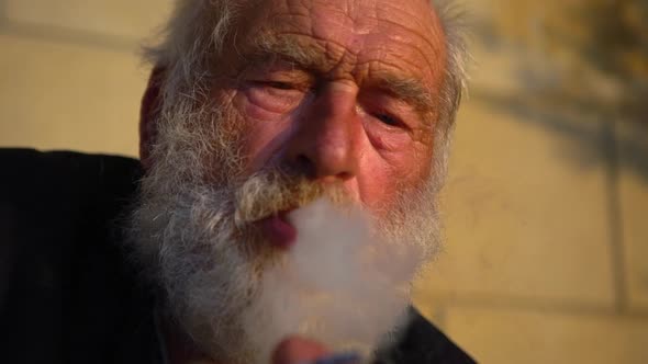 in Slow Motion Closeup Portrait of Old White Bearded Man Smoking Cigarette Smiling Looking Ahead on