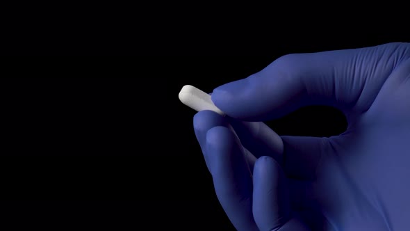 doctor holds a white pill with his fingers in blue medical protective gloves 