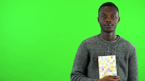 A Young Black Man Holds a Colorful Book in Front of His Chest and Smiles - Green Screen Studio