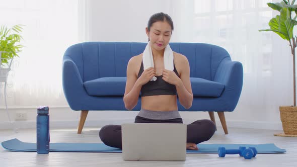 Athlete Asian young woman take a break during exercise online class on exercise mat at home