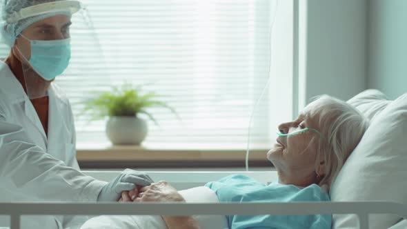 Doctor in Protective Uniform Supporting Elderly Patient in Hospital