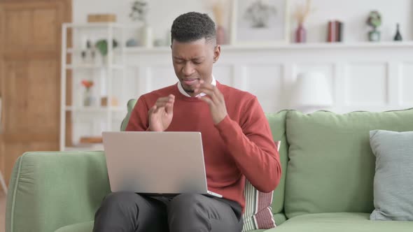African Man with Laptop having Headache on Sofa