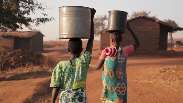 African women in a rural village carry water in buckets on their heads. Malawi, Africa.