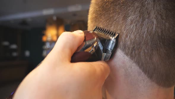 Hands of Hairstylist Cutting Hair of His Client with Electric Razor in Barbershop. Arms of