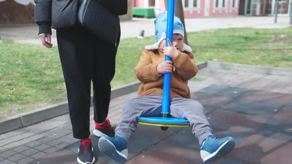 A Boy on a Playground in an Autumn Park Rides on a Swing in Cloudy Weather