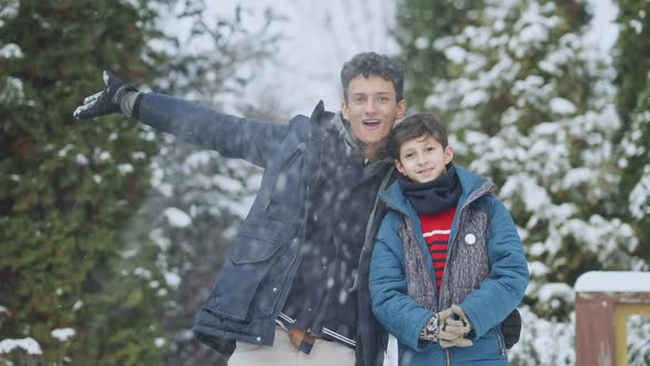 Middle Shot of Positive Teenage and Little Brothers Tossing Snow in Slow Motion Looking at Camera