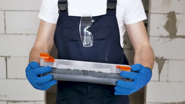 A Handsome Male Construction Worker Opens a Toolbox Against a Brick Wall