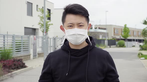 A Young Asian Man Takes Off His Face Mask and Looks at the Camera in an Empty Suburban Area