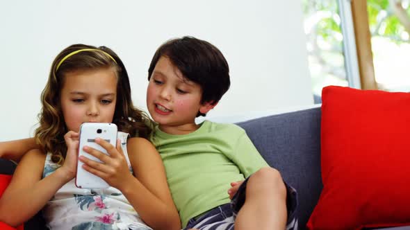 Siblings using mobile phone in living room