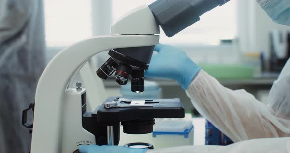 A Scientist in Sterile Clothing Looks Through a Microscope