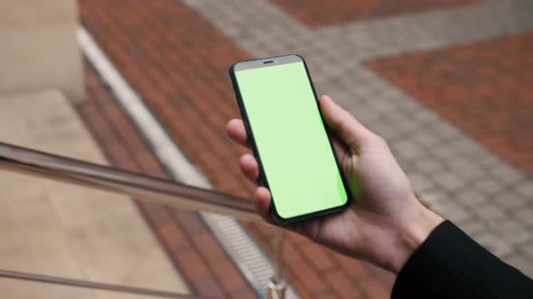 Close-up View of a Person Holding a Smartphone Swiping Pages on Mockup Green Screen Outdoor.