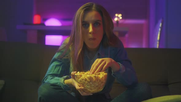 A Shocked Young Girl with Popcorn Is Watching a Tv Program or Movie at Night
