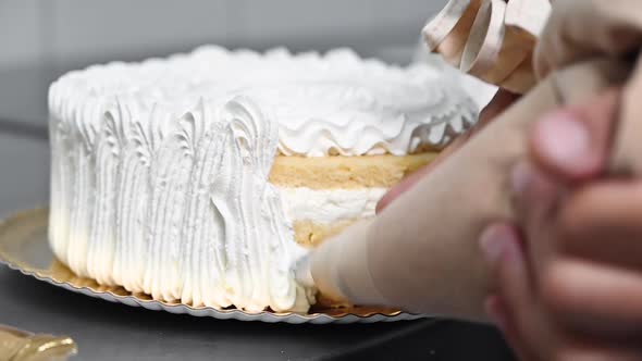 Pastry Chef Decorating Cake in Bakery Shop with a Pastry Bag with Cream