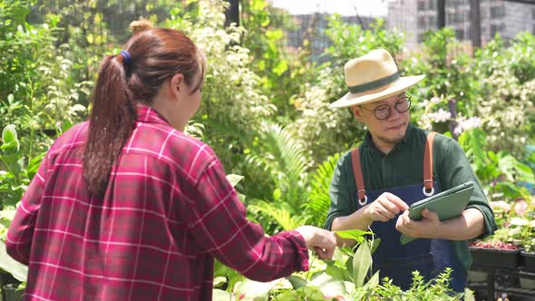 4K Asian man plant shop owner helping woman customer choosing potted plants in store