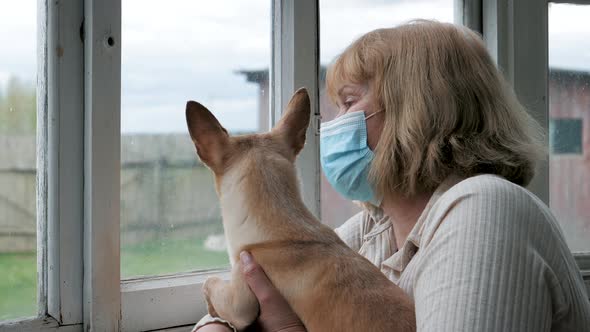 Woman In Medical Mask With Dog Looks Hopelessly Out Of Window At Quarantine