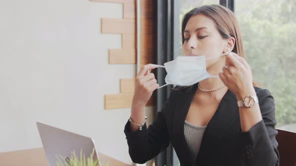 business woman wear medical face mask is self quarantine, uses a laptop while sitting at a table in