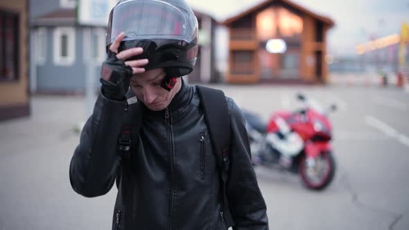 Young smiling biker takes off his helmet on the background of his motorcycle