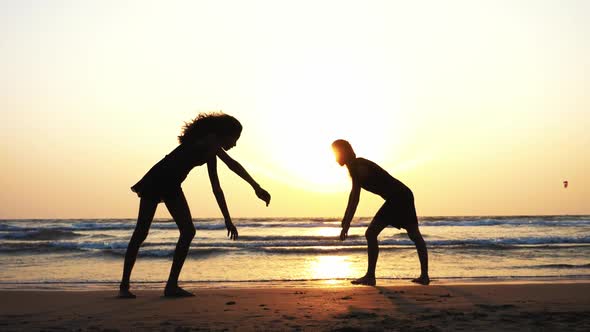 Silhouette of Sporty Young Women Practicing Acrobatic Element on the Beach