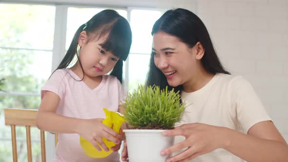Asian family mom and daughter watering plant in gardening near window at house.