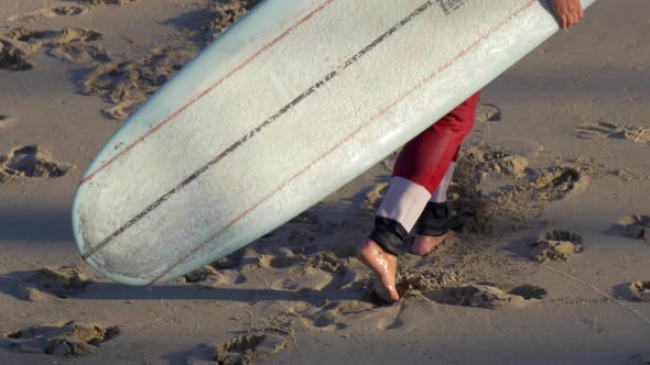 Santa Claus walking with his surfboard to go surfing at the beach.