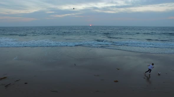 Aerial shot of little boy playing soccer on the beach at sunset.