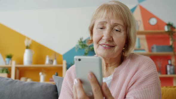 Slow Motion of Happy Old Woman Watching Online Content on Smartphone Screen Indoors