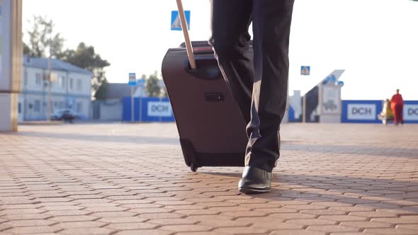 Close Up of Feet of Successful Businessman Walking Near Terminal and Pulling Suitcase on Wheels