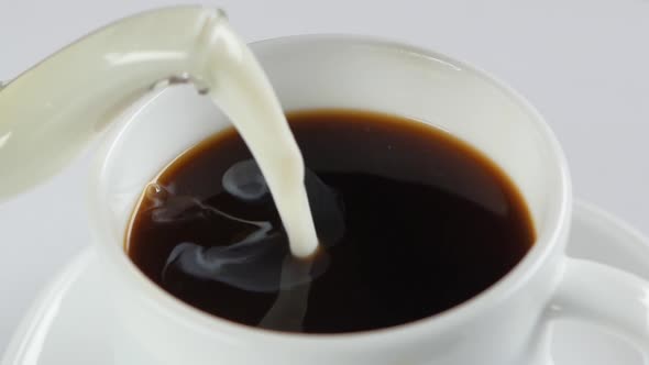 Pouring Milk Into Cup with Coffee on a White Background, Slow Motion, Close Up