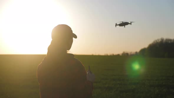 Silhouette of a Girl Farmer Using a Drone in a Wheat Field at Sunset. Concept Technology Innovations