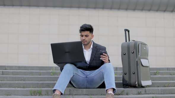 Handsome Arabian Man in Stylish Wear Sitting on Stairs and Working on Wireless Laptop While Waiting