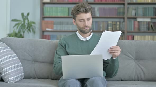 Serious Man Studying Documents and Working on Laptop