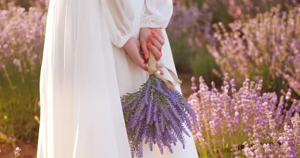 a Gentle Girl in a White Light Dress Holds a Bouquet of Lavender Flowers