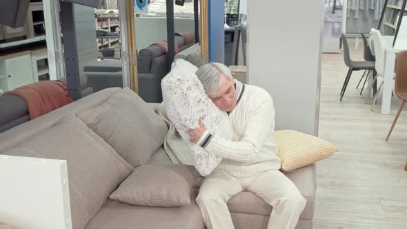 Cheerful Elderly Man Trying Soft Cushions on Sale at Furniture Store