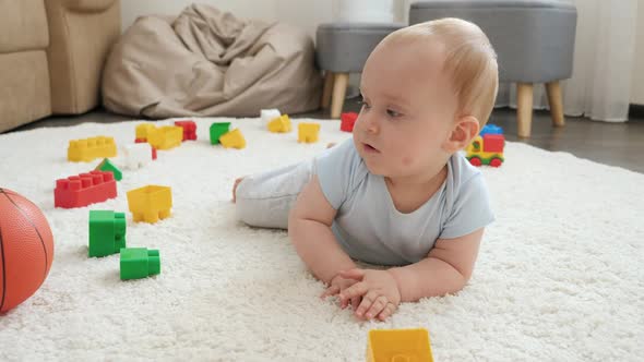 Cute Baby Boy Lying on Carpet and Palying with Basketball Ball and Toys