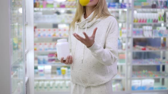 Unrecognizable Smiling Pregnant Woman Juggling Lemon Standing with Vitamin Pills Bottle at Shelves