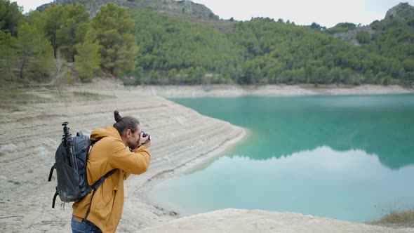 Young Man with Backpack Takes Pictures of Lake and Forest in Spain