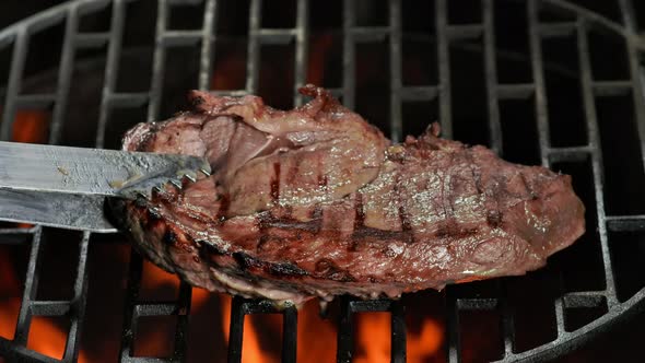 Kitchen Tongs Are Flipping a Beef Steak Lay on the Grill Grid