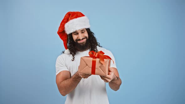 Young Curious Man in Santa Hat Got Christmas Present Shaking It Listening What Rattles in Gift Box