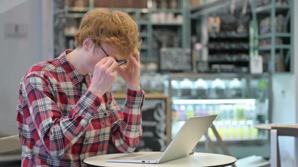 Young Redhead Man with Headache Using Laptop in Cafe