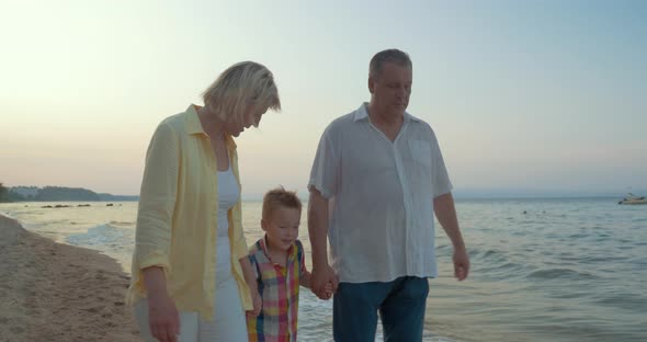 Grandparents and little grandchild walking on the beach