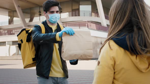 Courier Wearing Protective Mask and Gloves Gives Delivery Package to Customer Outdoors in the City