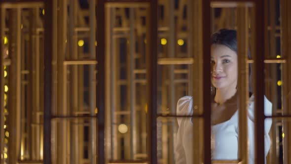 Beautiful Asian woman walking along a wall of windows with a stunning look and smmile at the camera