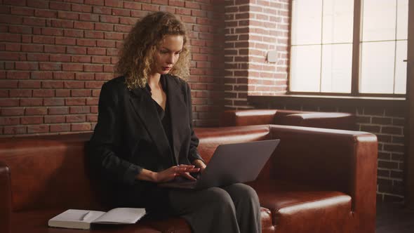 Young Stylish Businesswoman Working on a Laptop in a Loft Apartment with Red Brick Wall