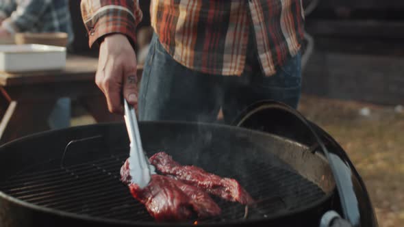 Man Placing Meat Steak on Grill with Tongues