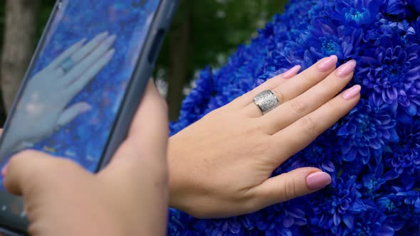 A Woman Photographs Her Hand with a Beautiful Manicure Against a Background of Bright Blue Flowers