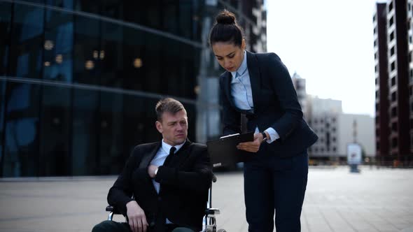 Young Cripple Business Man in Wheelchair Communicates with His Colleague About Documents Textpad