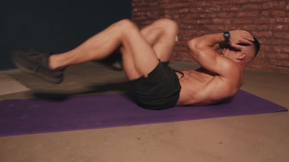 Young Man with a Naked Torso Training in the Room on a Sports Mat and Does an Exercise on the Press