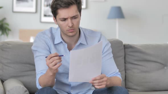 Handsome Young Man Reading Documents While Sitting on Couch